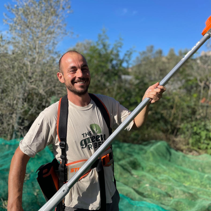 Man holding a long tool in an outdoor setting with greenery